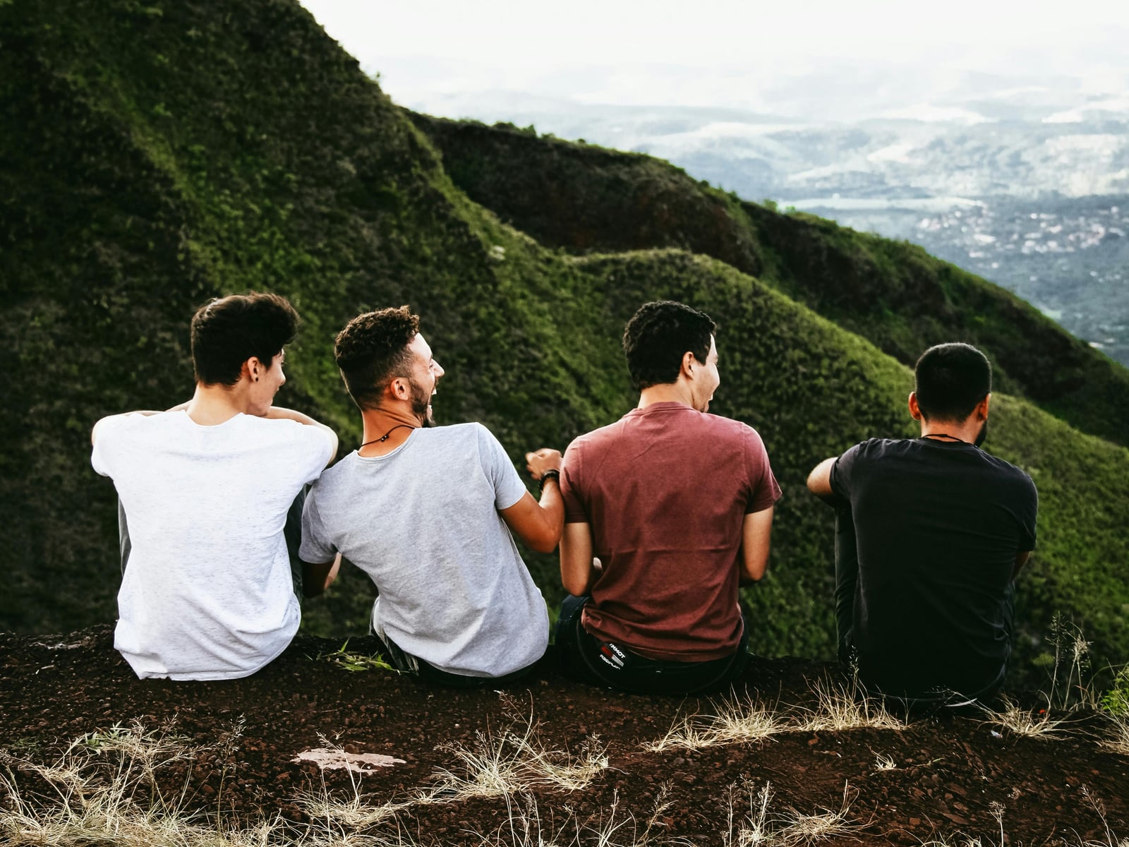 A small group sitting together on a hillside at sunset, looking out over a wide valley.
